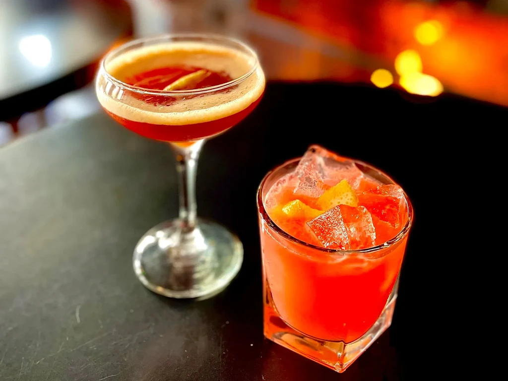 Two red cocktails, one in a coupe glass and one in a rocks glass.