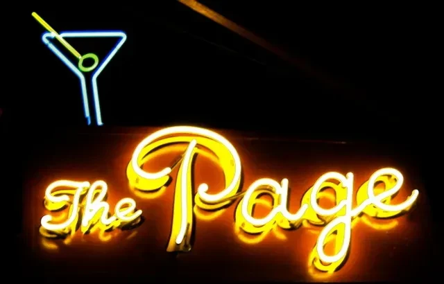 Neon martini glass and "The Page" sign in yellow on a dark background.