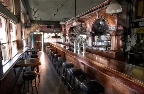 Long, narrow bar with stools, elk head, and ornate wooden backbar.
