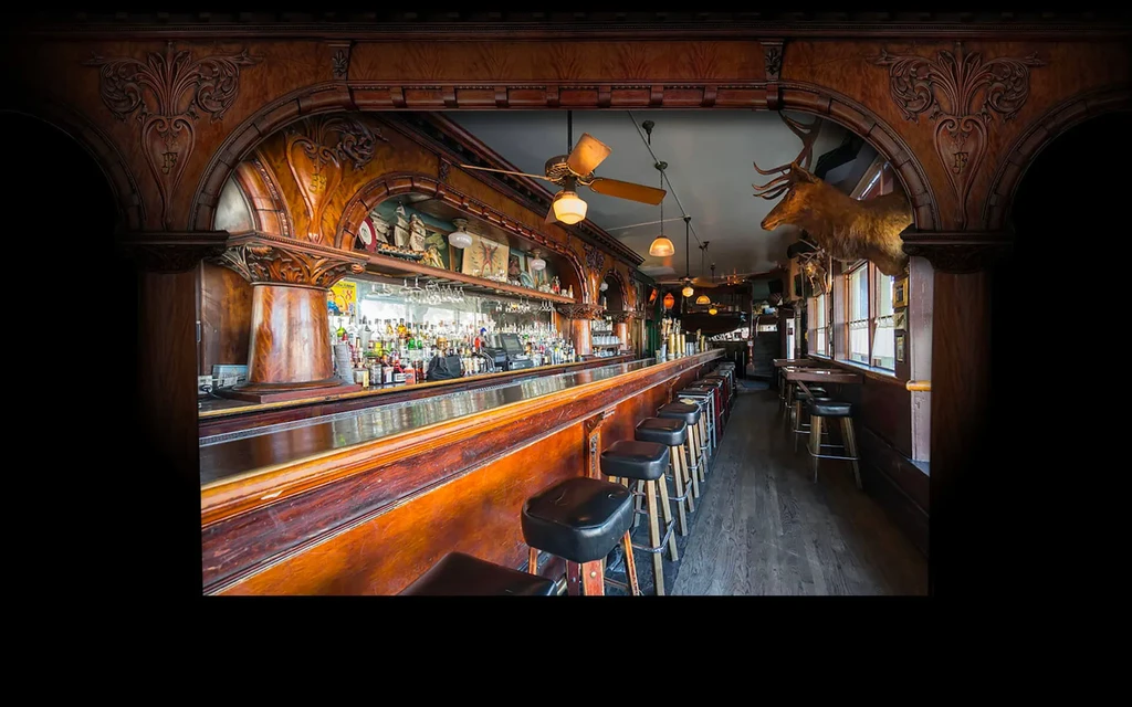 Long, narrow bar with ornate wooden archways, stools, and deer head mounts.