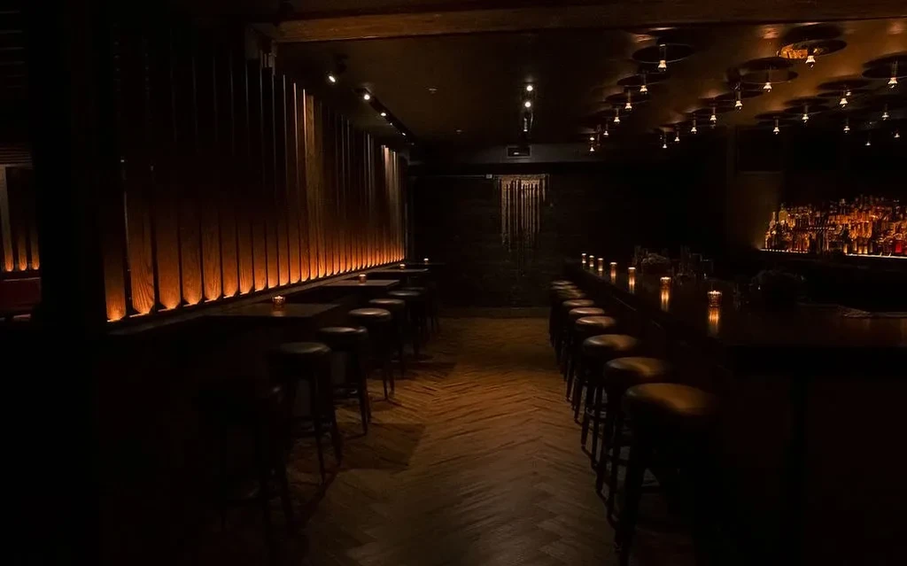 A dimly lit bar with a long counter and many stools.