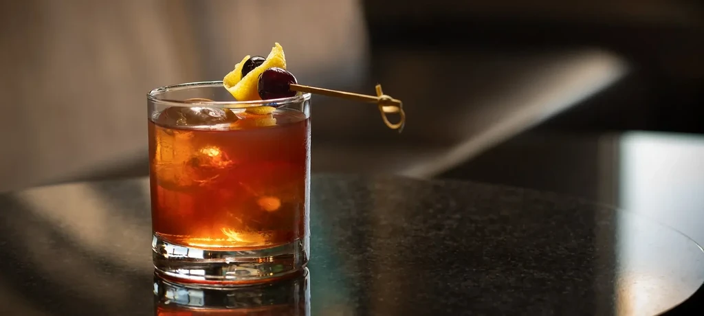 An Old Fashioned cocktail with cherry, orange peel, and ice.