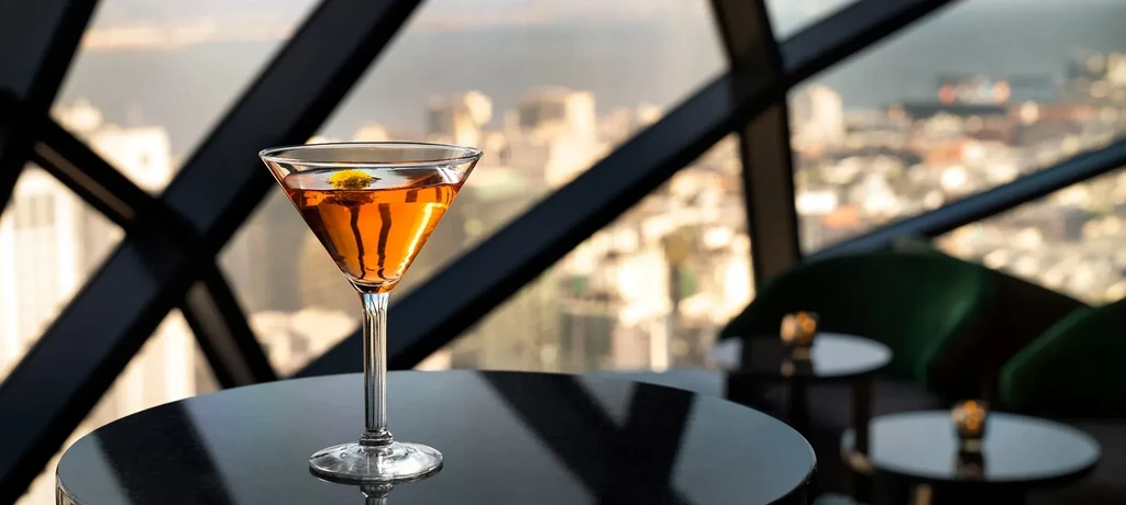 A martini glass on a table in a high-rise bar, cityscape background.