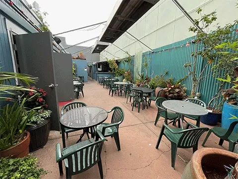 Outdoor patio with green tables and chairs under a translucent roof.