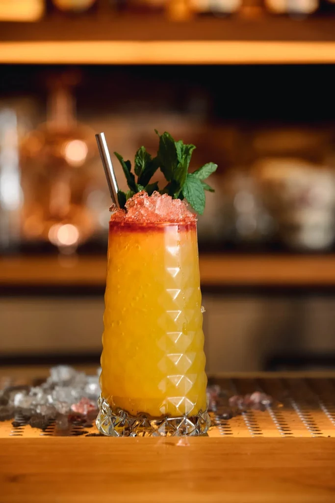 Tall glass with layered yellow and red drink, mint garnish, straw.