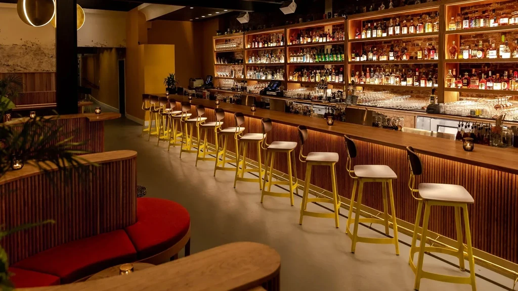 An empty modern bar with a long wooden counter and yellow bar stools.