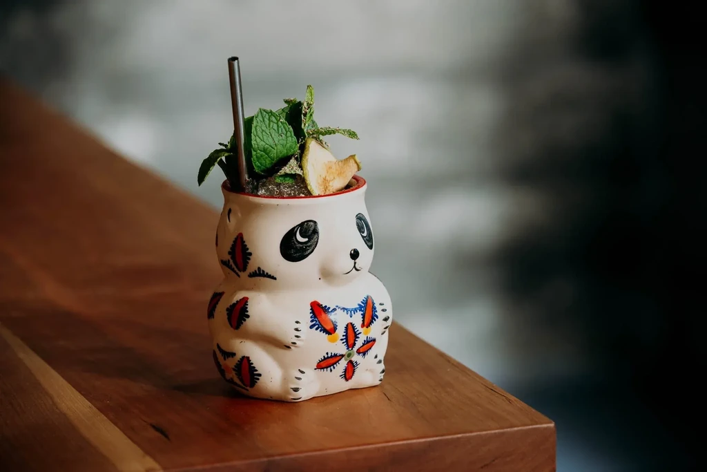 White panda-shaped cocktail glass with colorful designs, mint, and dried fruit.