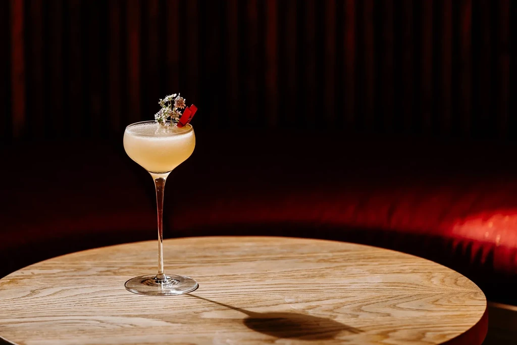 Light yellow cocktail garnished with flowers on a wooden table.