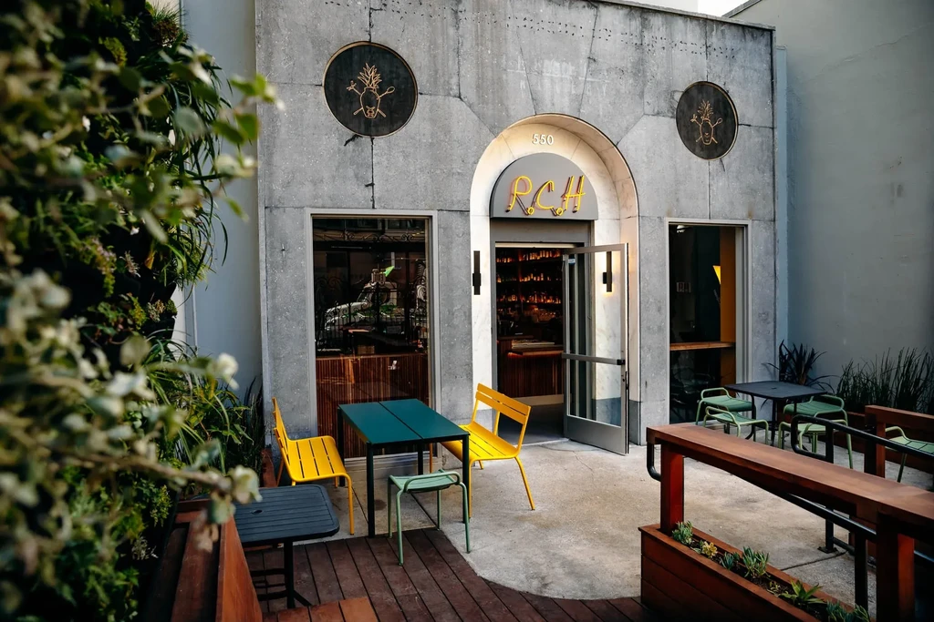 A cafe patio with yellow chairs and tables outside a stone building.