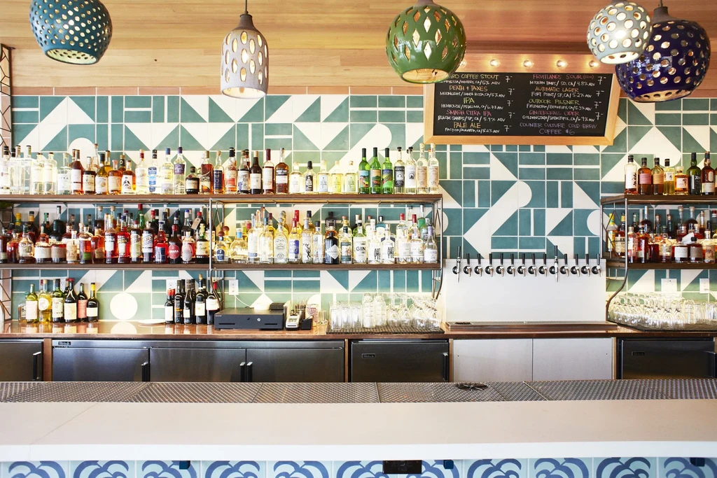 A well-stocked bar with green patterned tiles and hanging lamps.