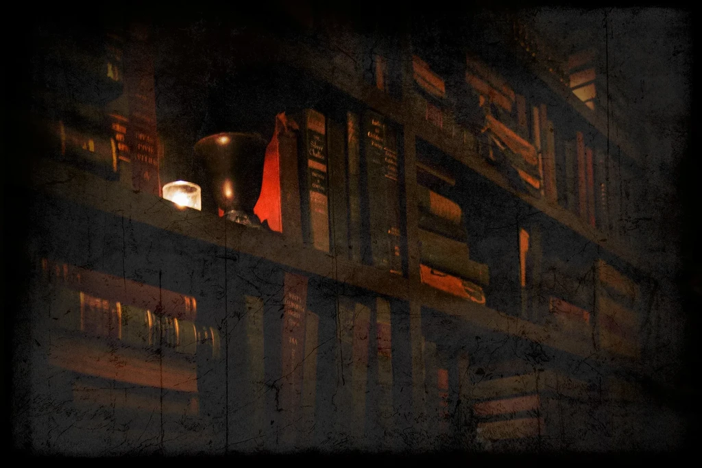 Shelves of old books dimly lit by a flickering candle and small cup.
