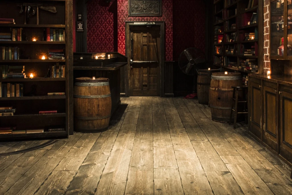 A dimly lit room with bookshelves, wooden barrels, and red wallpaper.