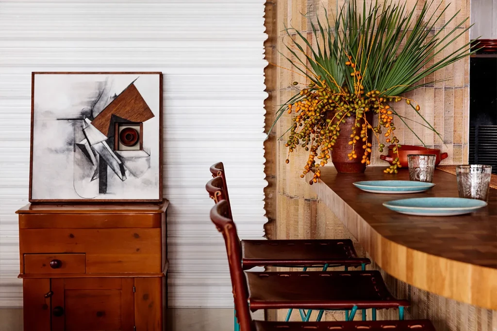 Modern artwork, a wooden cabinet, bar stools, and a plant display.