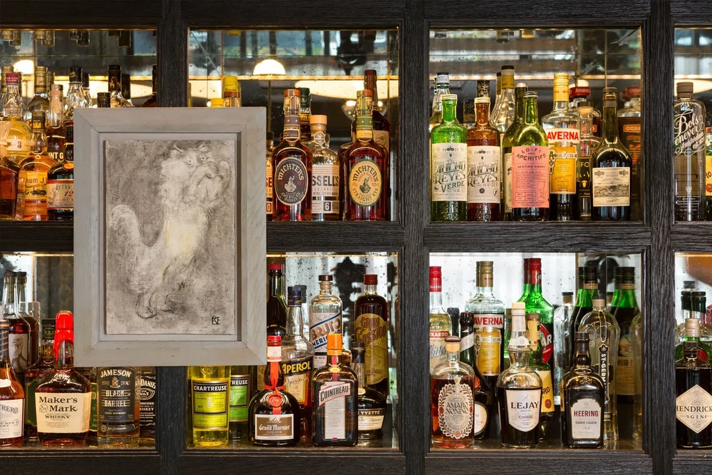 A painting of a white rooster in a gray frame, surrounded by liquor bottles.