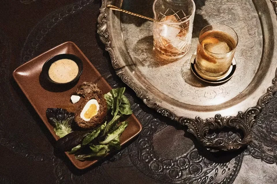 Scotch egg, sauce, and two cocktails on a silver platter.