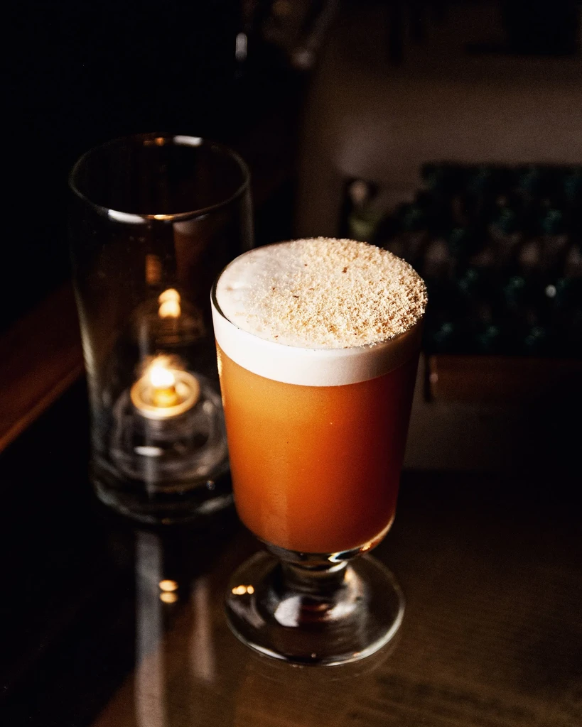 A foamy orange drink with sprinkled topping next to a lit candle.