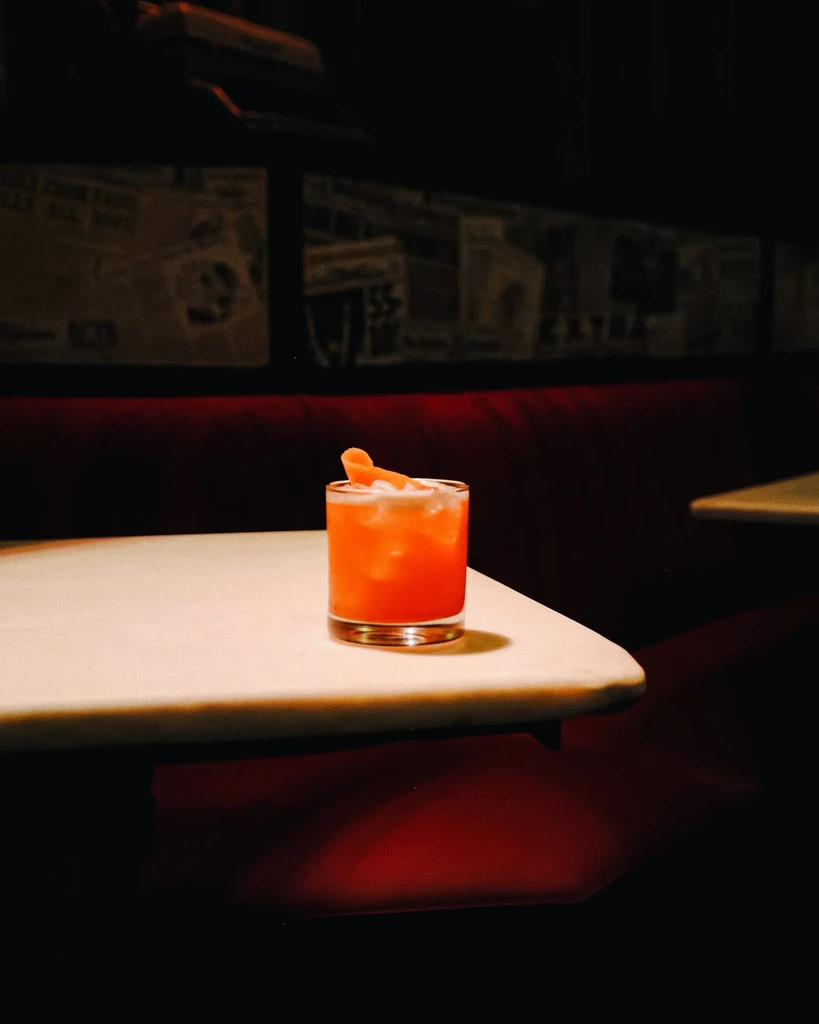 Orange cocktail with ice and an orange peel on a white table.