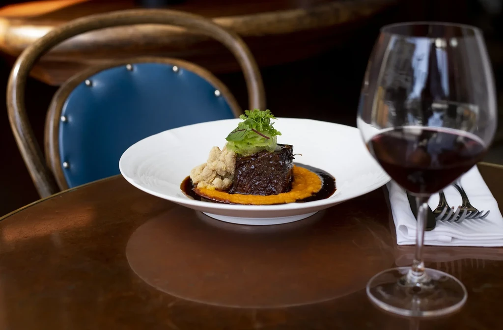 A gourmet dish with red wine on a polished wooden table.