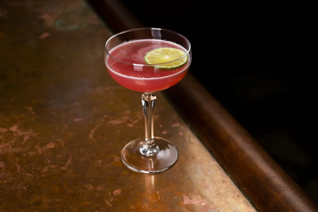 Pink cocktail with a lime slice on a copper bar top.