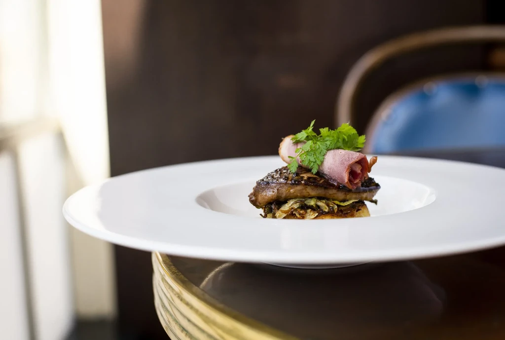 Garnished gourmet dish with meat, vegetables, and rolled ham on a white plate.
