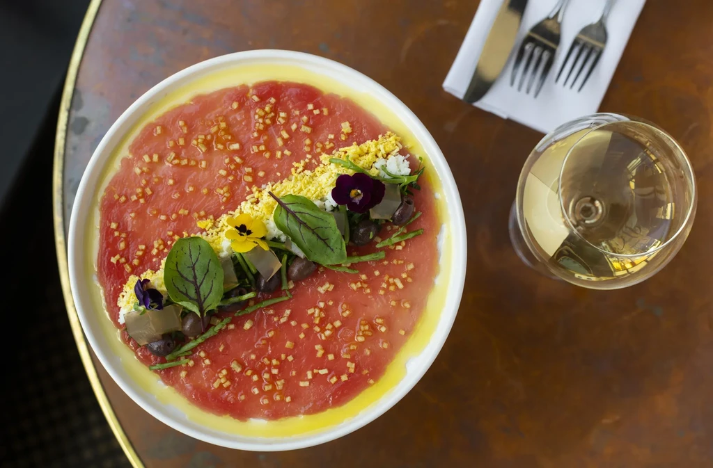 Overhead shot of a carpaccio dish with wine, napkin, and silverware.