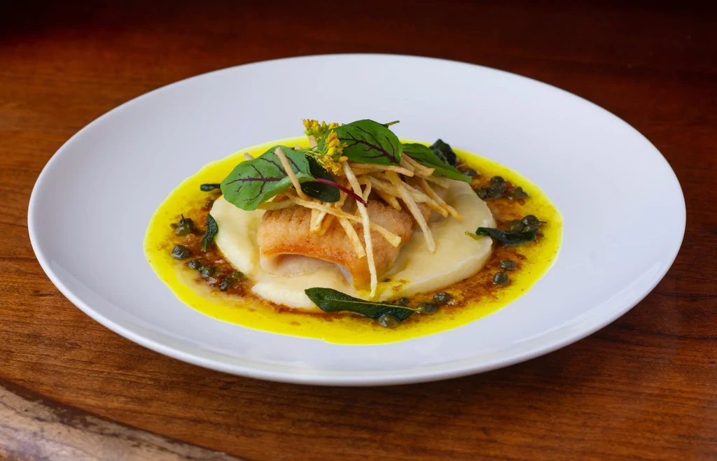 Pan-seared fish on mashed potatoes with yellow sauce, greens, and shoestring fries.