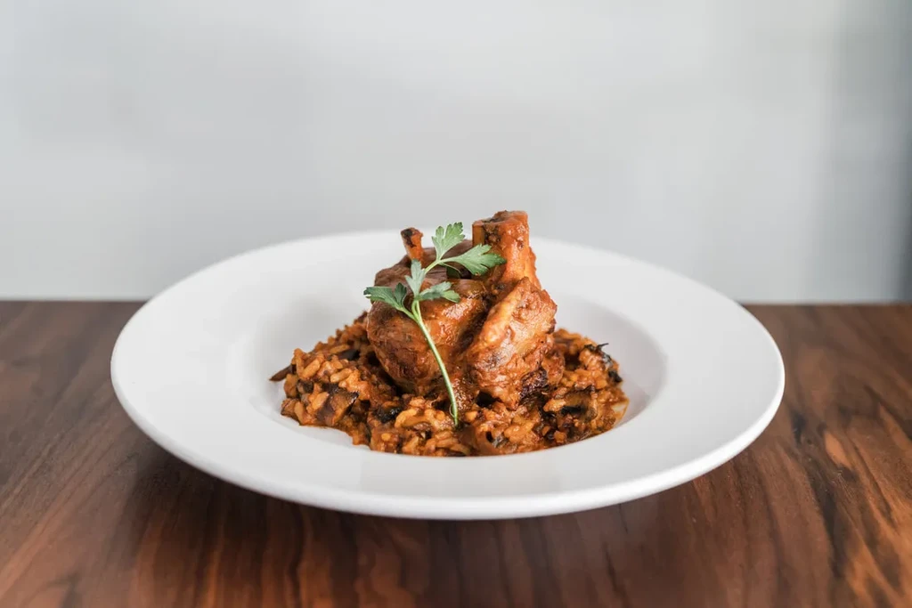 A white plate of osso buco with risotto, garnished with parsley.