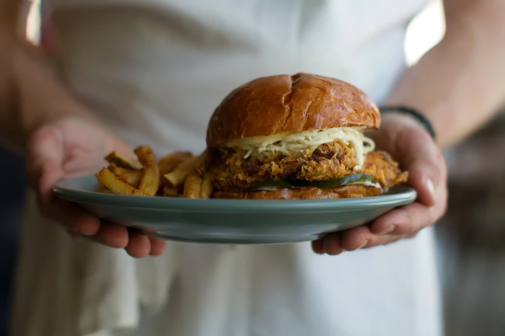 Person holding a plate with a crispy chicken sandwich and fries.