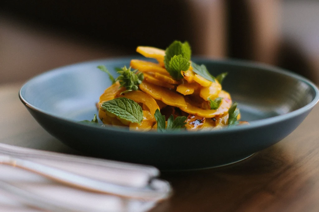 A teal bowl filled with thin, round slices of golden squash and mint.