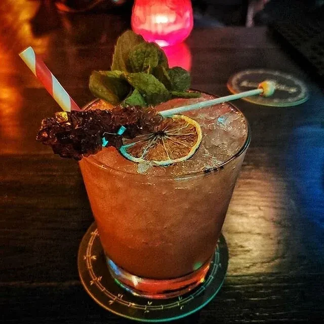 Cocktail with dried orange, rock candy, mint, and a striped straw.