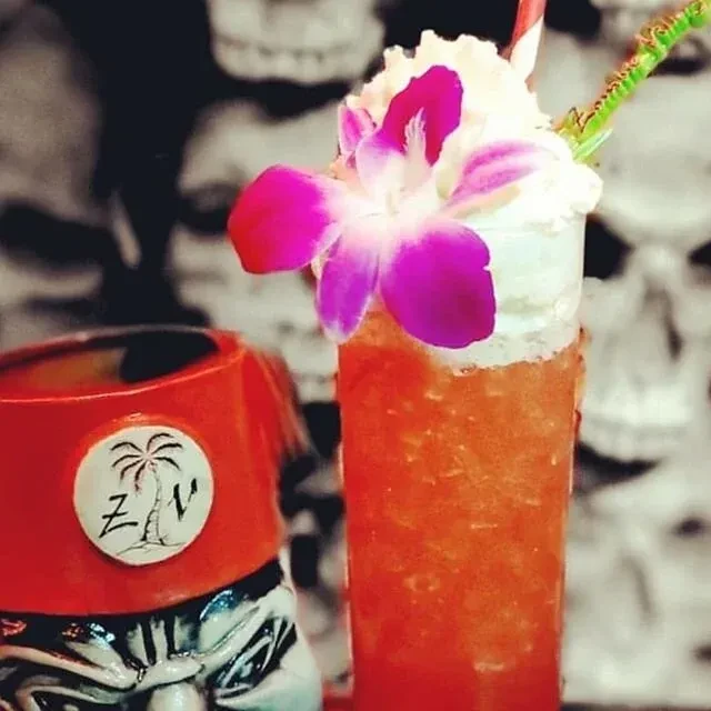 A red tiki mug and a garnished cocktail with a purple orchid.