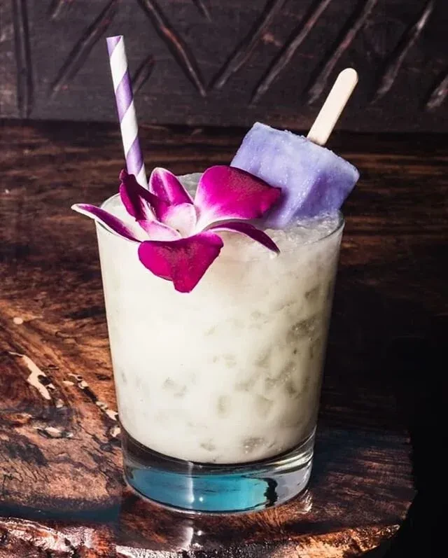 A cocktail with a purple orchid, striped straw, and purple popsicle.