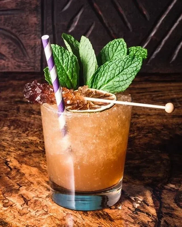 A cocktail garnished with mint, dried lime, sugar crystals, and a straw.