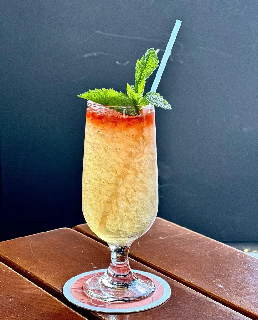 A clear glass with a cocktail, garnished with mint and a straw.