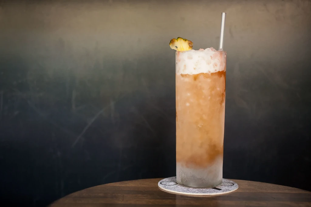 A tall, frosted cocktail with a pineapple slice and straw.