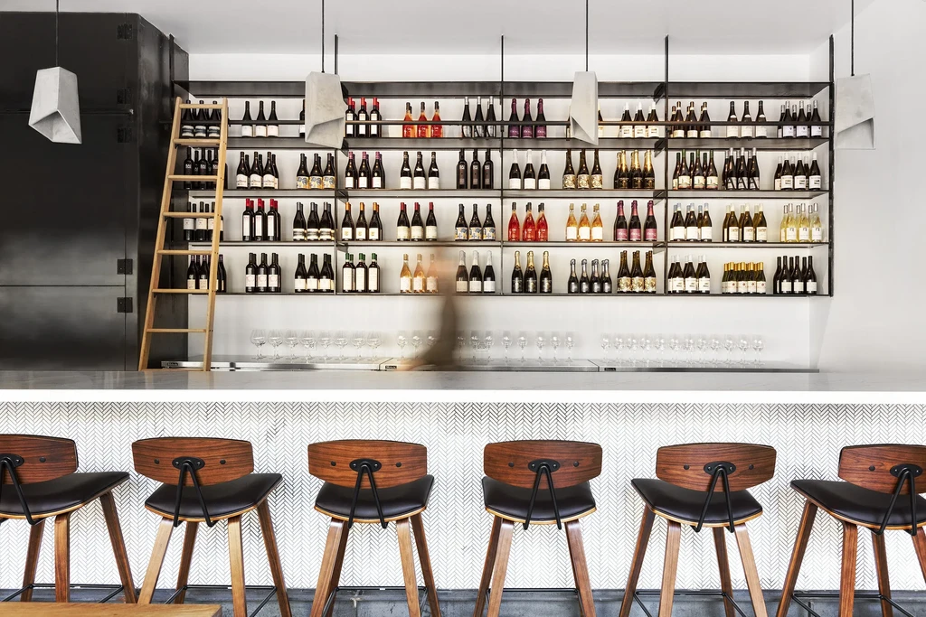 A modern wine bar with bottles on shelves and stools in the foreground.