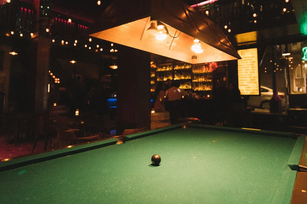 A pool table with an 8-ball and an illuminated bar in the background.