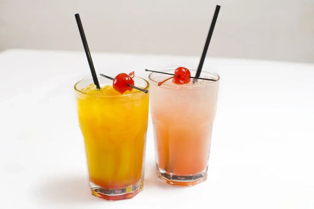 Two tall glasses with orange drinks, straws, and cherry garnishes.