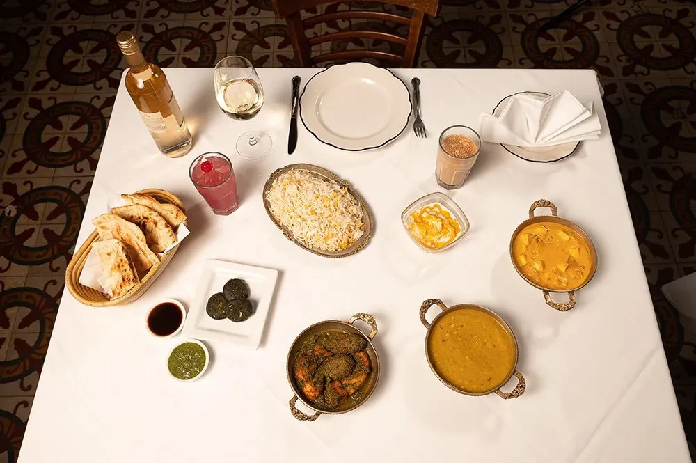 Overhead view of an Indian meal with various dishes on a white tablecloth.