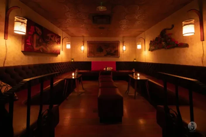 Dimly lit, cozy lounge with U-shaped booths and a long central bench.