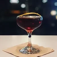 Dark red cocktail in a stemmed glass with a lemon twist.