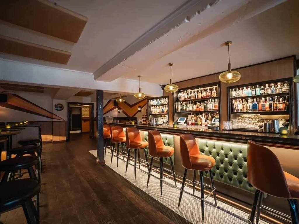 A modern bar with orange stools and a fully stocked back bar.