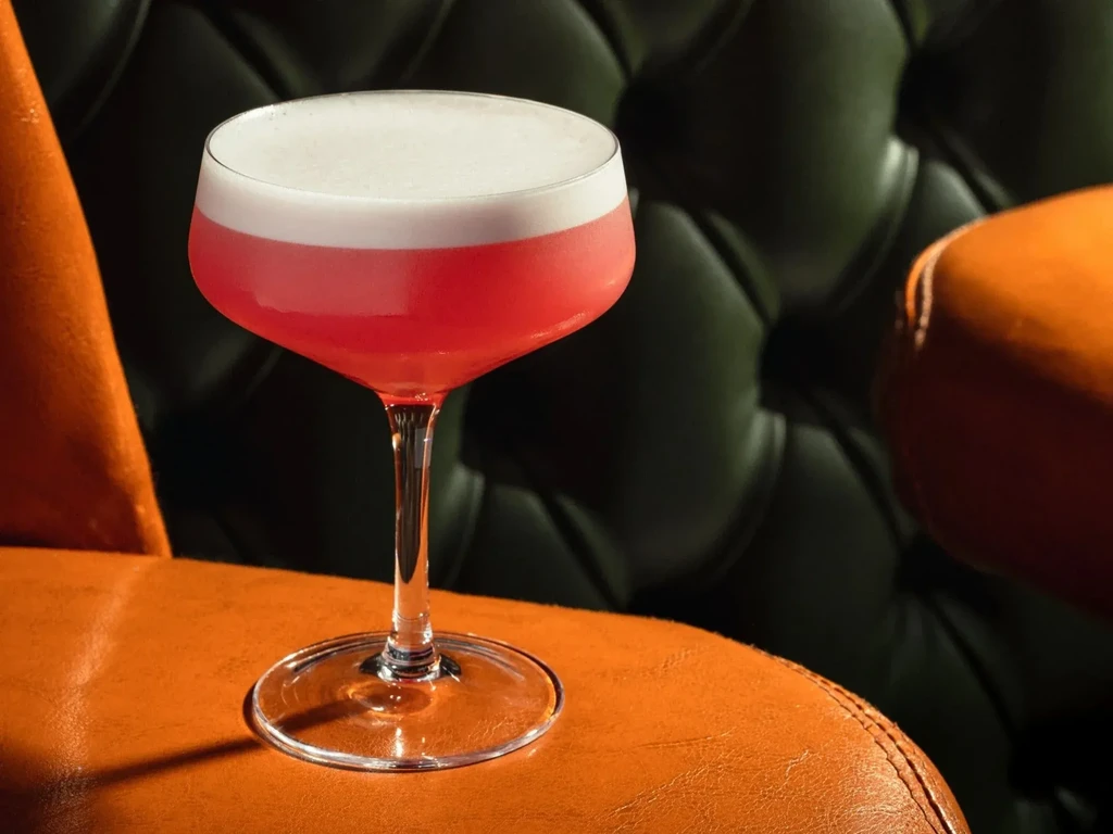 A pink cocktail with foam, on a brown leather chair.