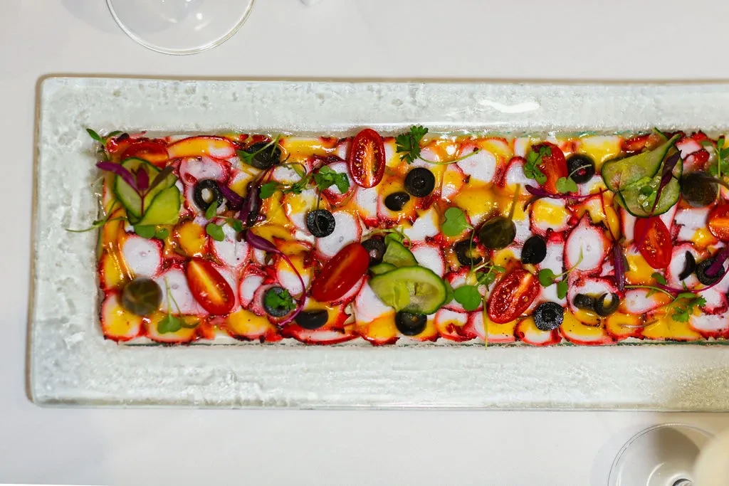 Overhead view of an octopus carpaccio dish with vegetables on a plate.
