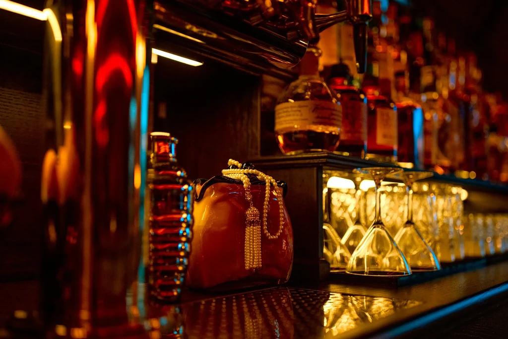 A dark bar counter with bottles, glasses, and a decorative pearl necklace.
