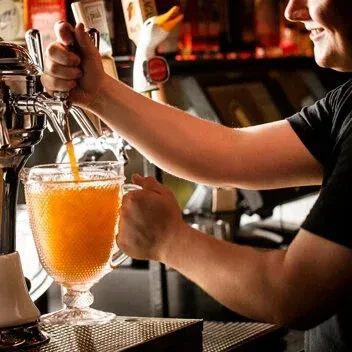 Bartender pours an orange drink from a tap into a glass.