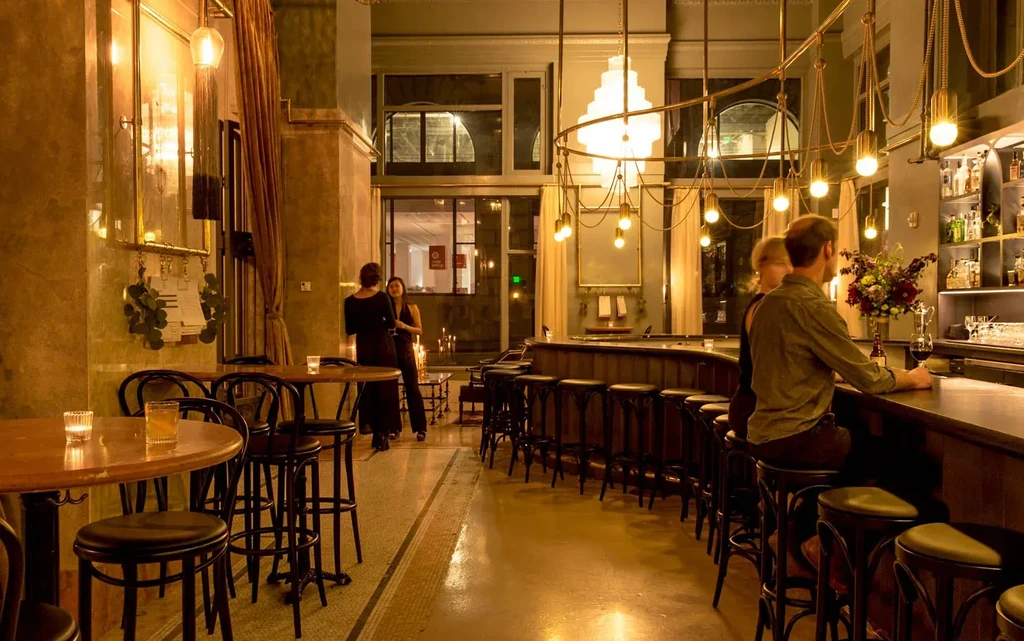 People drinking at a well-lit bar with a long counter and tables.