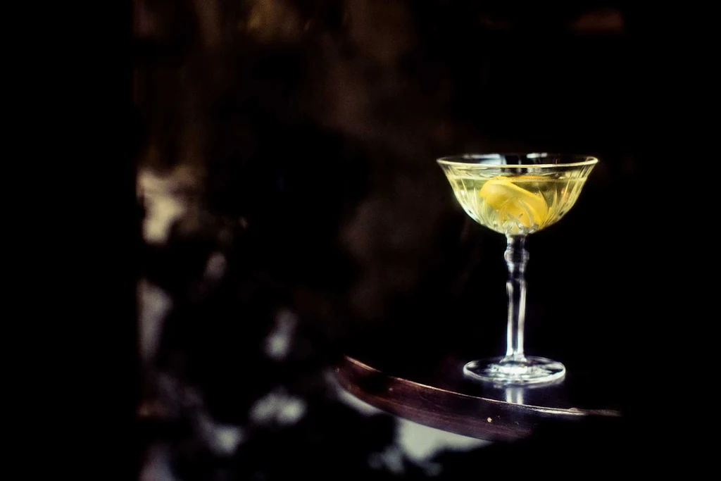 A cocktail glass with a lemon peel on a dark wooden table.