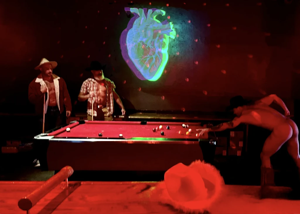 Three men playing pool, one nude, with a heart projected on the wall.