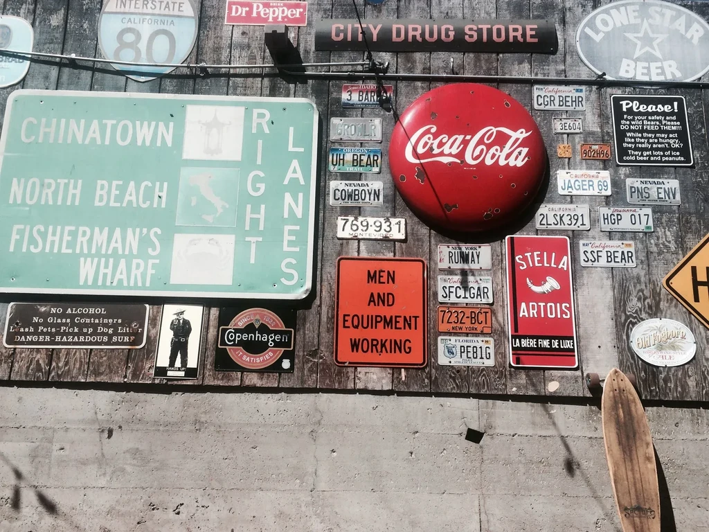 A weathered wall with signs, license plates, and a large red Coca-Cola button.